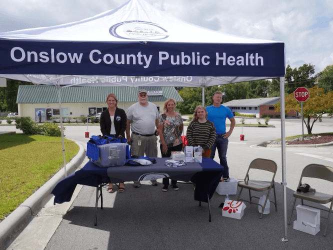 Onslow County Public Health booth/tent with volunteers standing behind a table