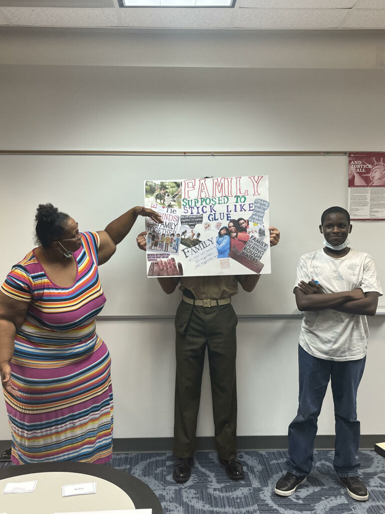 Mother pointing to a poster explaining their concept while husband and son stand beside her.